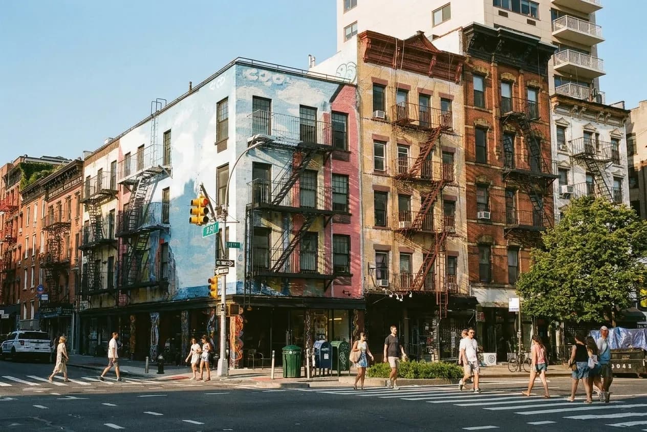East Village street corner with painted tenement facades and fire escapes in late-afternoon summer light