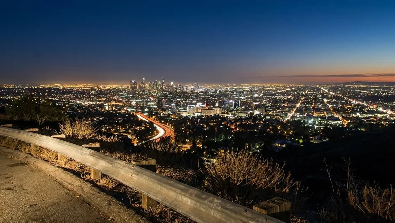 City lights spread across a basin seen from a hillside road at night