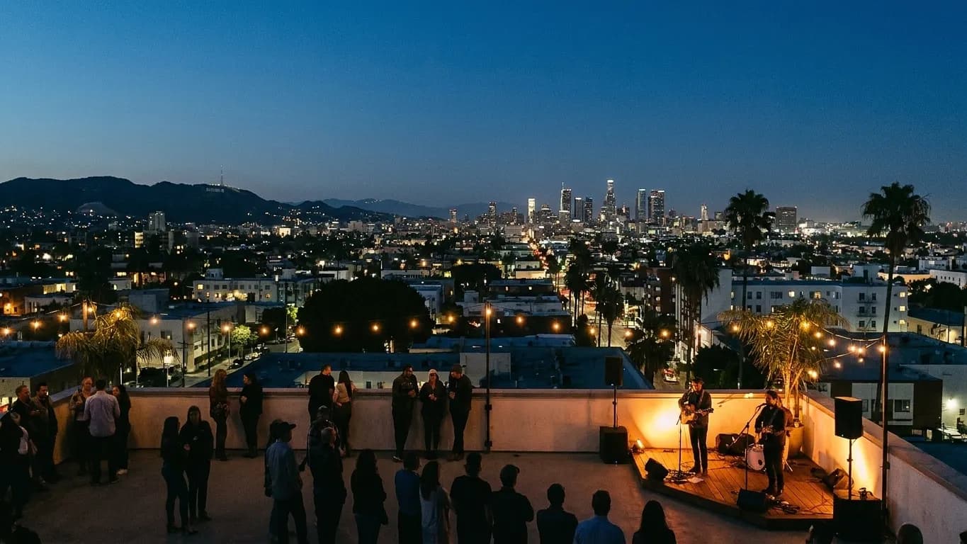 A rooftop gathering in Los Angeles at night under strung bulbs with the lit city grid beyond