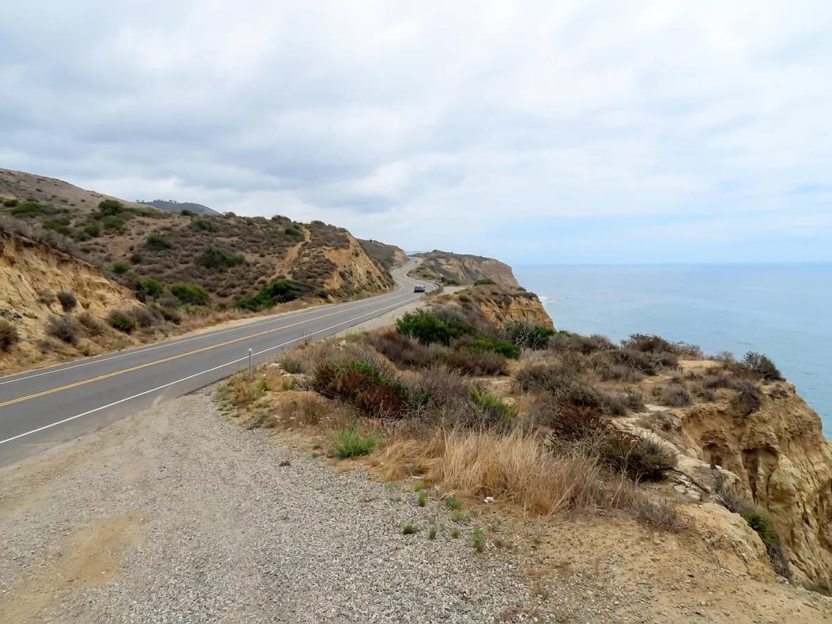 A two-lane coastal highway curving along a cliff edge above the ocean north of Los Angeles