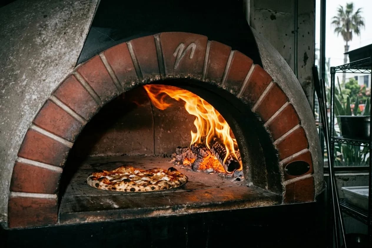 Flames inside a domed pizza oven with a pizza at the mouth