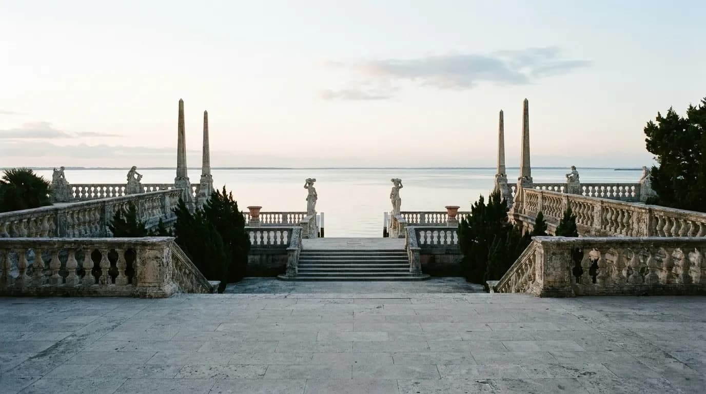 A formal stone terrace stepping down to open bay water, carved balustrades and cypress-like planting on either side, flat morning light across the stone