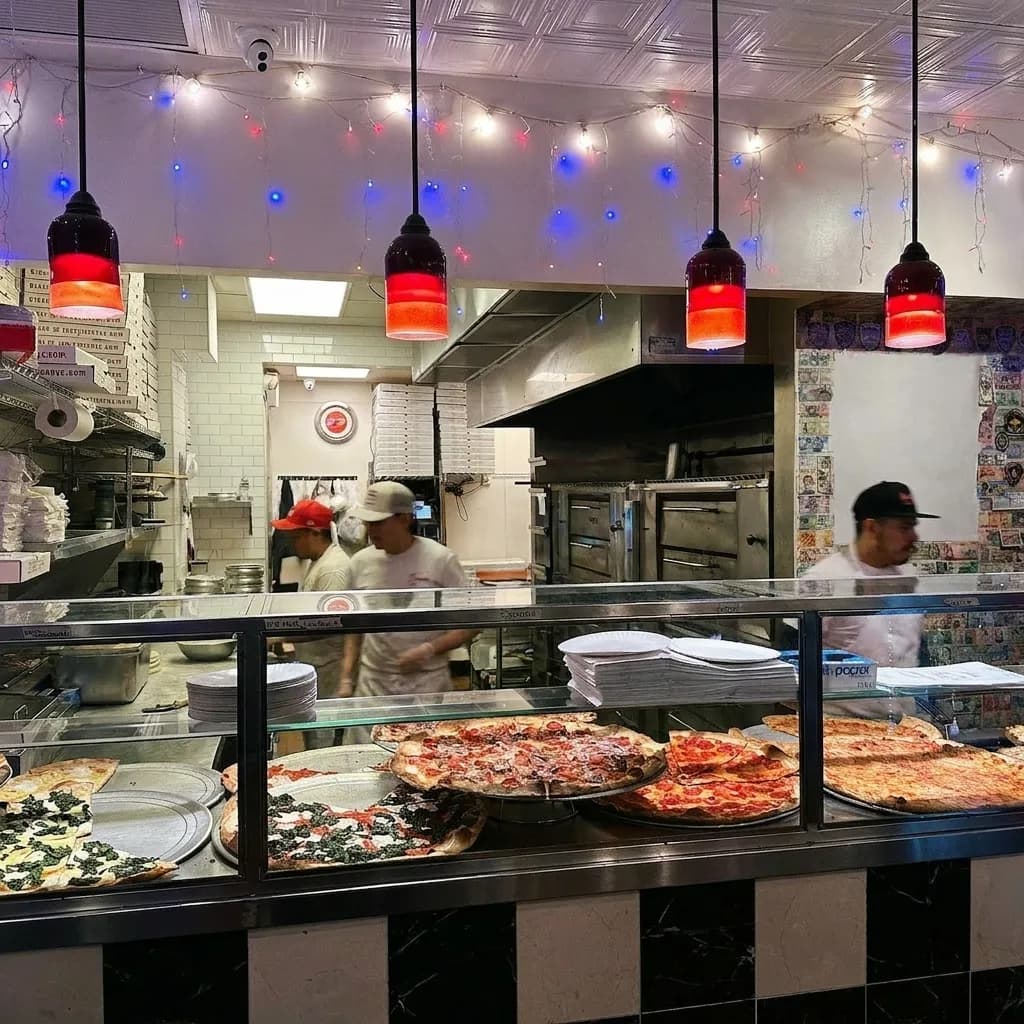 Glass slice counter inside a classic Greenwich Village pizzeria with whole pies on steel trays