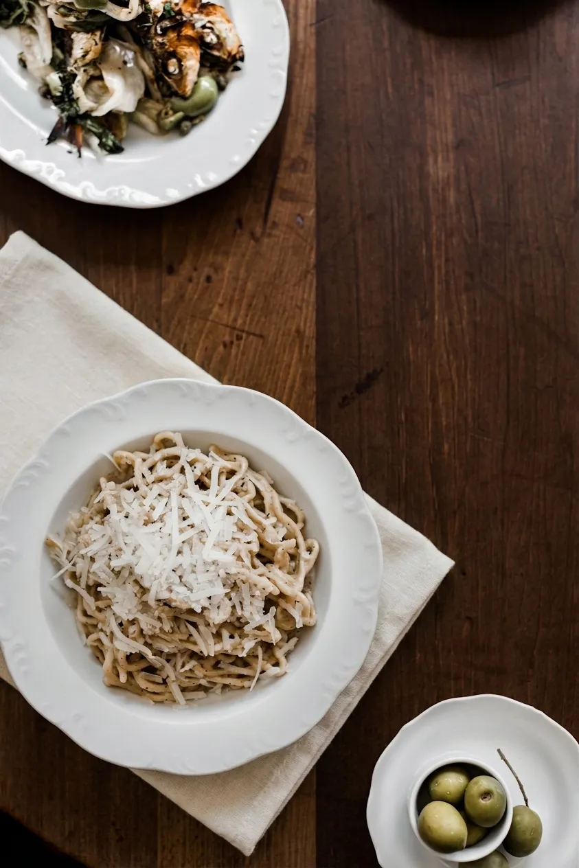 Overhead view of tonnarelli cacio e pepe with shaved pecorino and charred vegetables on a dark wood trattoria table in the West Village