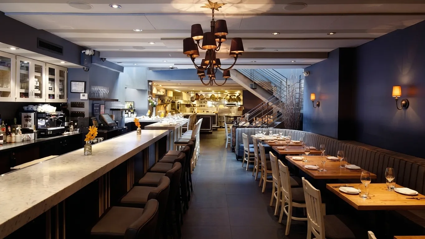 Marble bar counter with stools leading toward the open kitchen inside a West Village Italian restaurant at evening