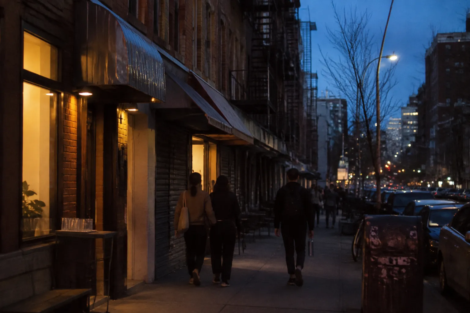 Orchard Street in the Lower East Side at dusk with lit storefronts and pedestrians