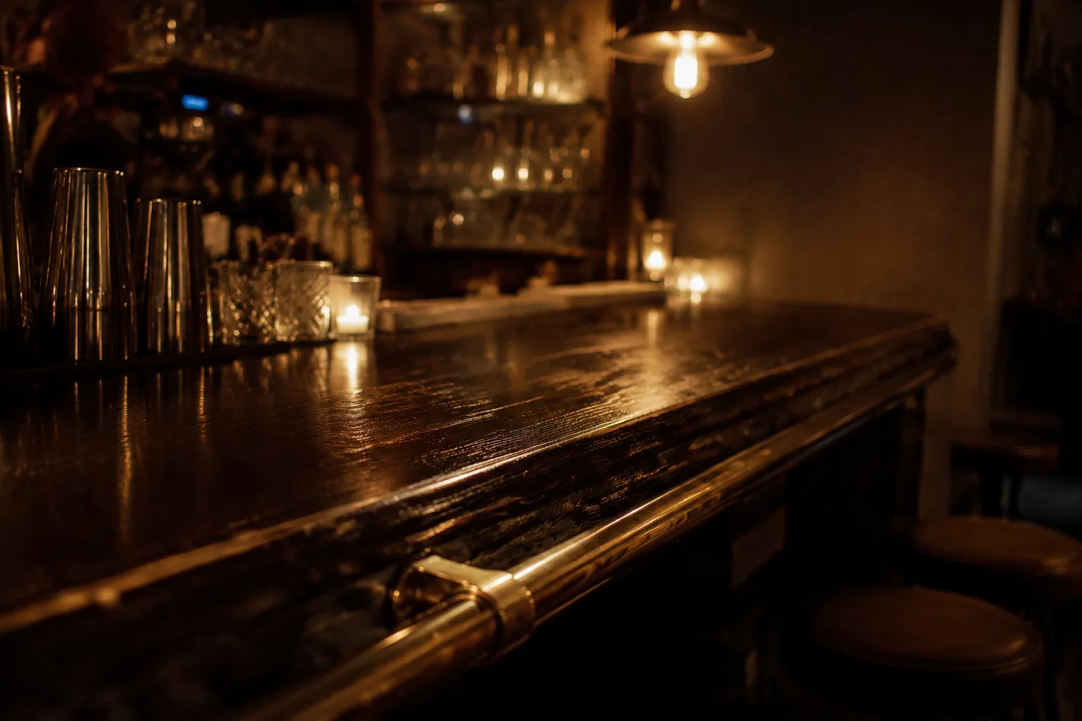 Worn wooden bar counter with brass rail in dimly lit West Village cocktail bar