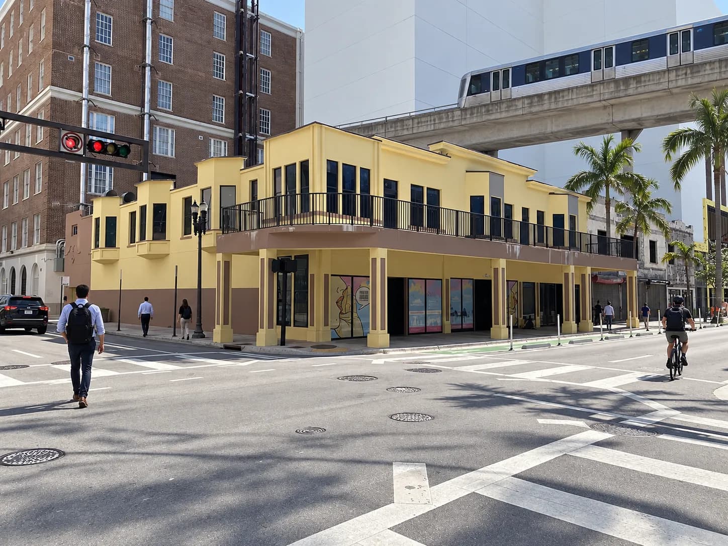 Downtown street with older low-rise buildings and newer towers behind, an elevated transit guideway crossing overhead and palms along the pavement