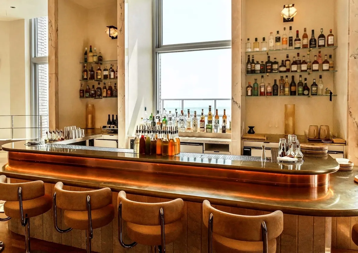 Brass-topped bar counter with leather stools and backlit bottle shelves inside an award-winning Manhattan restaurant