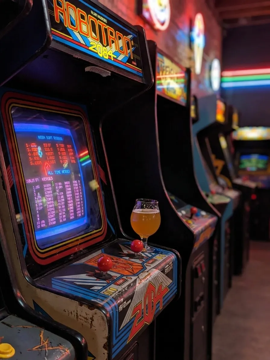 Vintage arcade cabinet glowing beside craft beer glass at Barcade Highland Park