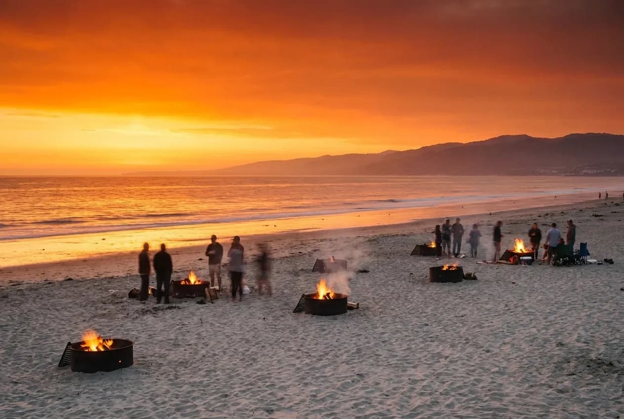 Fire rings on a Los Angeles beach at sunset with groups gathered around small fires