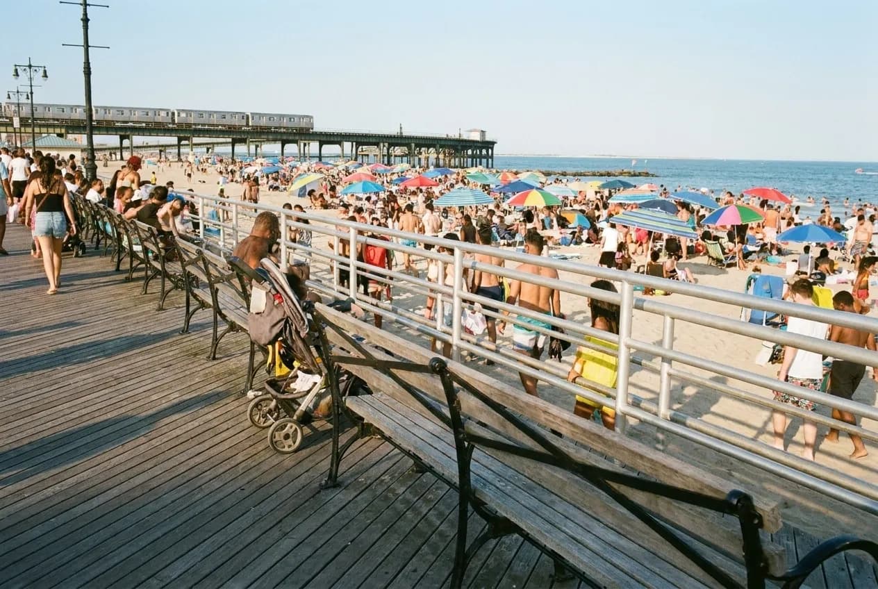 Boardwalk approaching Coney Island beach with subway infrastructure visible in the distance
