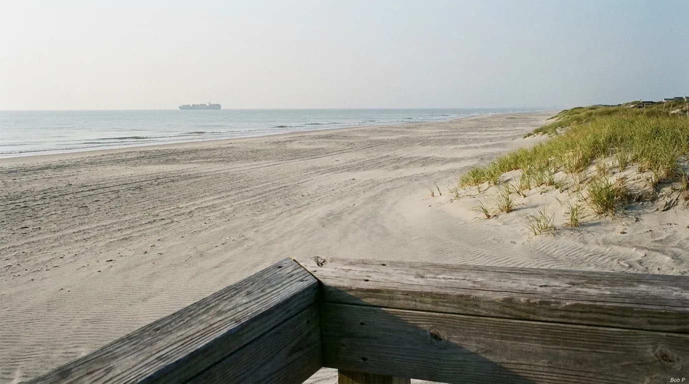 A wide empty beach at mid-morning with a boardwalk edge and low dunes running into haze