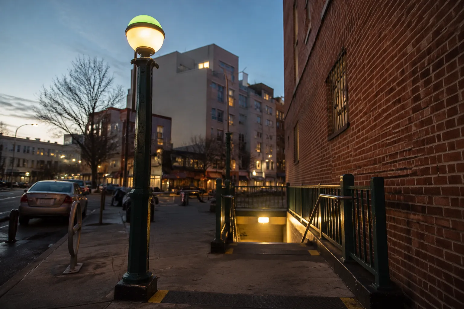 Greenpoint Avenue subway entrance at dusk with storefronts along Manhattan Avenue in Brooklyn