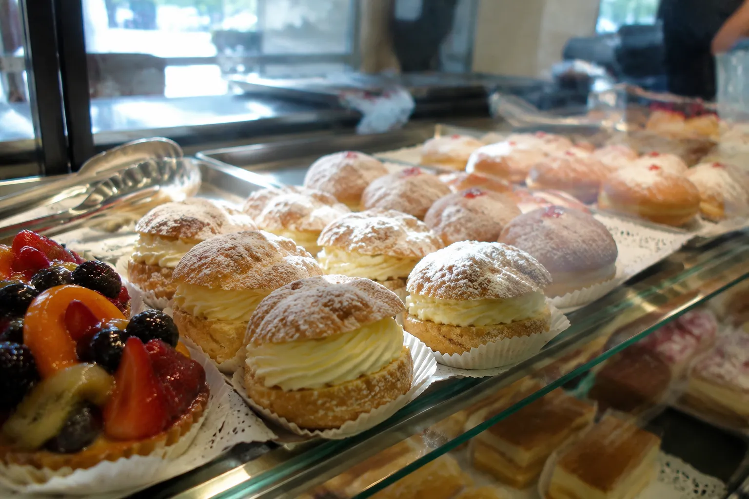 Pastry display case in a traditional Polish bakery showing cream pastries and fruit tarts