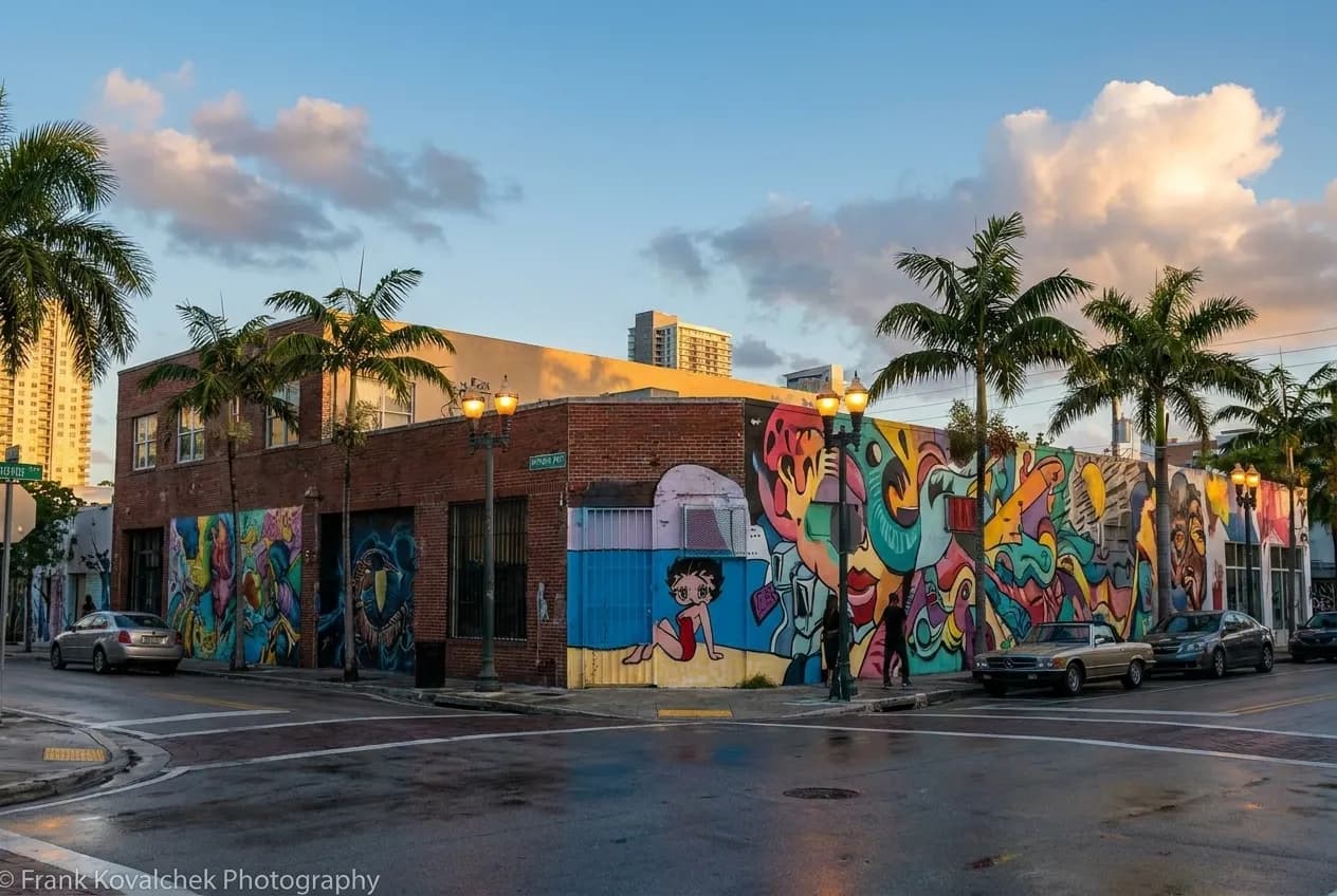 A Wynwood Miami street corner at dusk with colorful murals and parked cars along the avenue