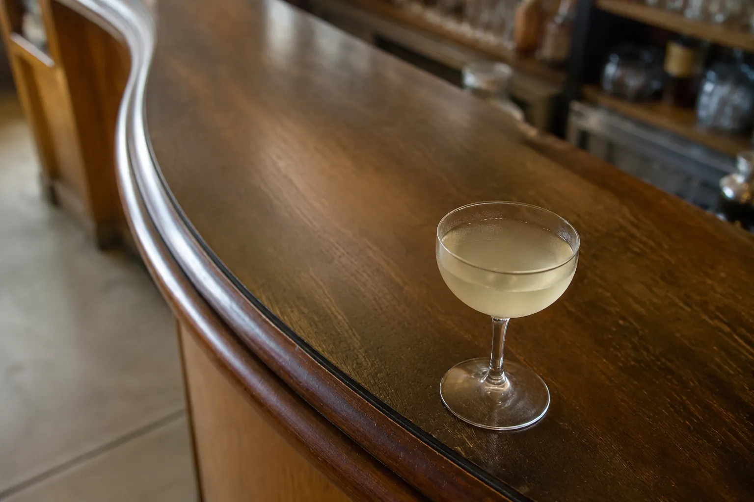 Close-up of a cocktail glass on a polished wooden bar with soft afternoon light