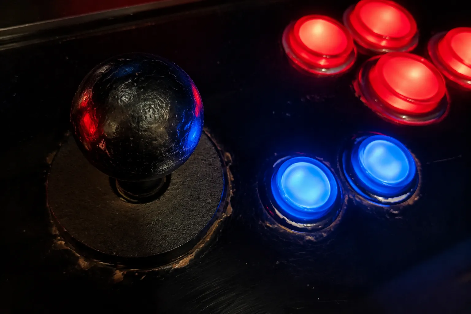 Close-up of arcade game joystick and illuminated buttons with worn surfaces