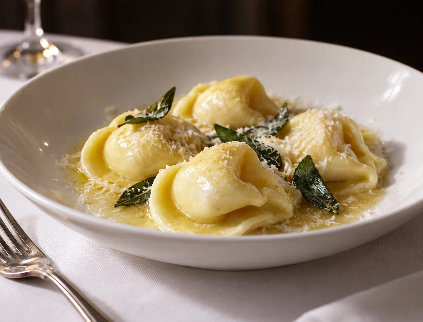 A shallow bowl of filled pasta parcels in a pale butter sauce, dusted with grated cheese