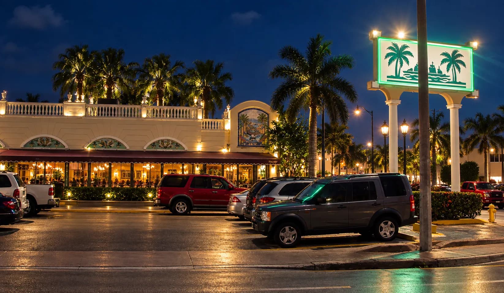 The illuminated exterior of a large Cuban restaurant on a Miami boulevard at night, green and white signage glowing above a row of glass doors and parked cars