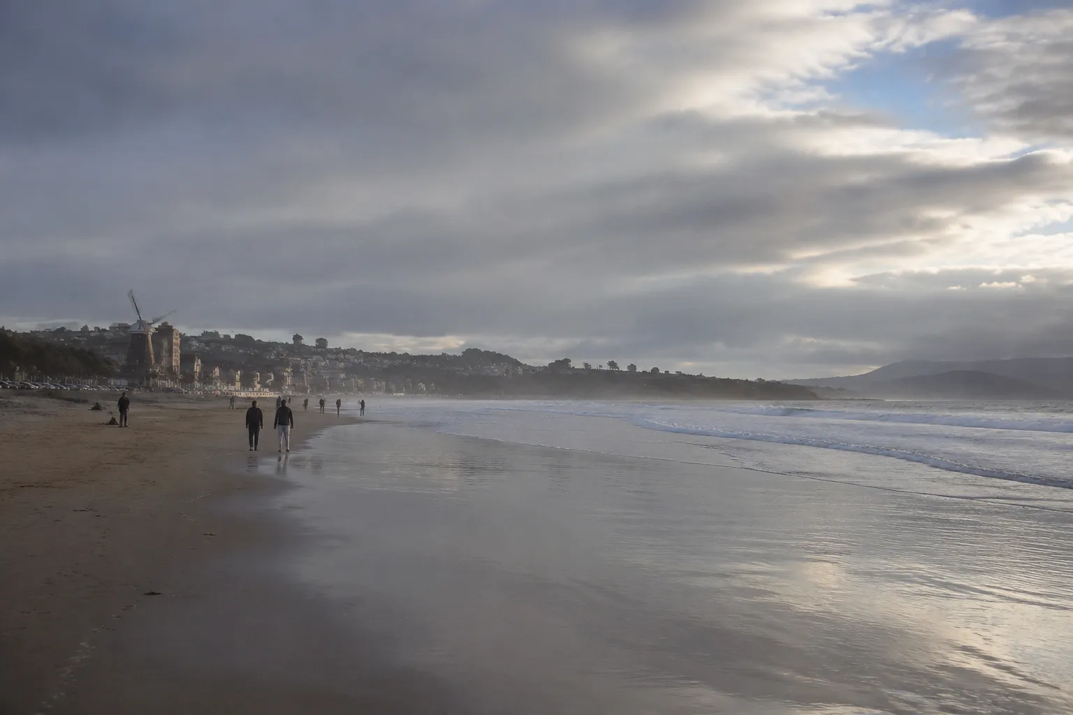 Late afternoon light on Ocean Beach with wet sand, breaking fog, and distant walkers along the San Francisco shoreline