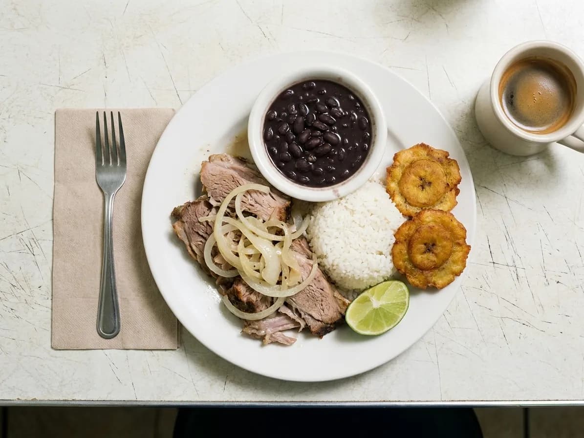 A Cuban lunch plate of roast pork, rice, black beans and fried plantain on a worn formica counter