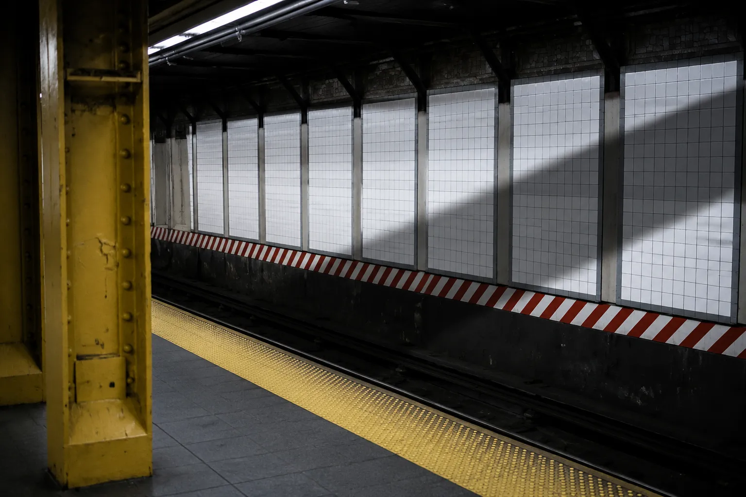Union Square subway platform edge with white tile wall and yellow safety stripe