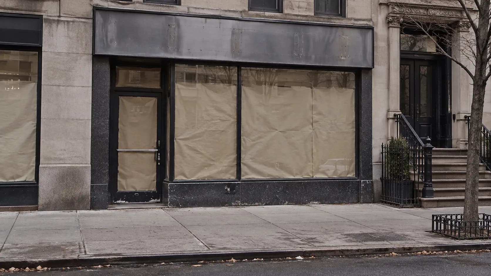 An empty shopfront with papered windows on a quiet Manhattan street in daylight