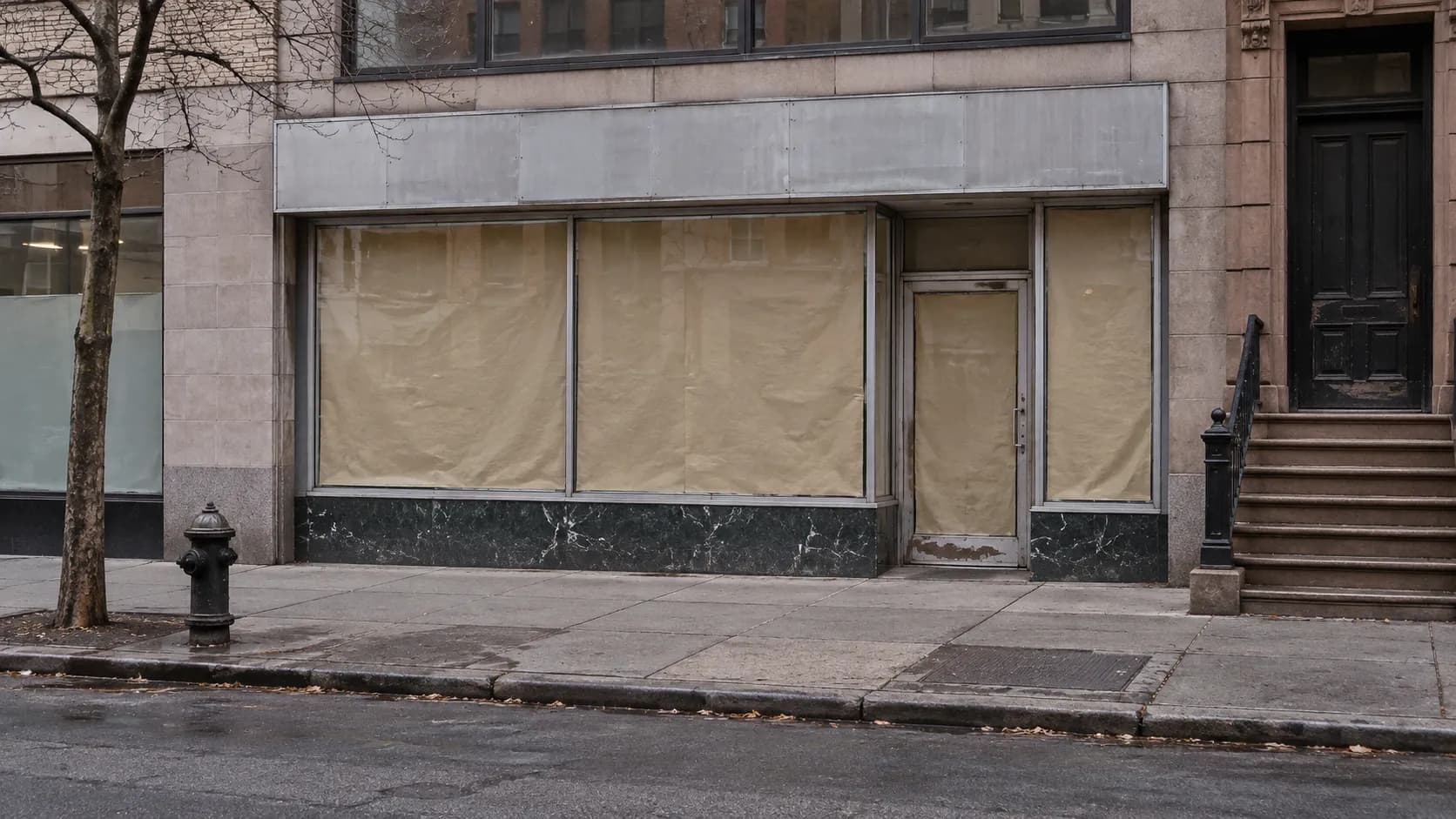 An empty shopfront with papered windows on a quiet Manhattan street in daylight