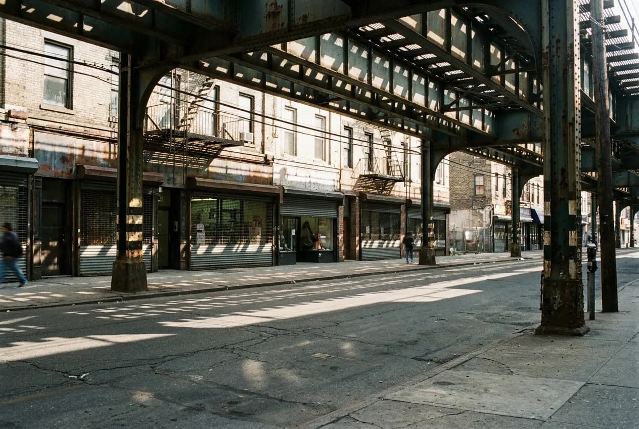 Elevated train line casting shadows over a commercial avenue in Queens
