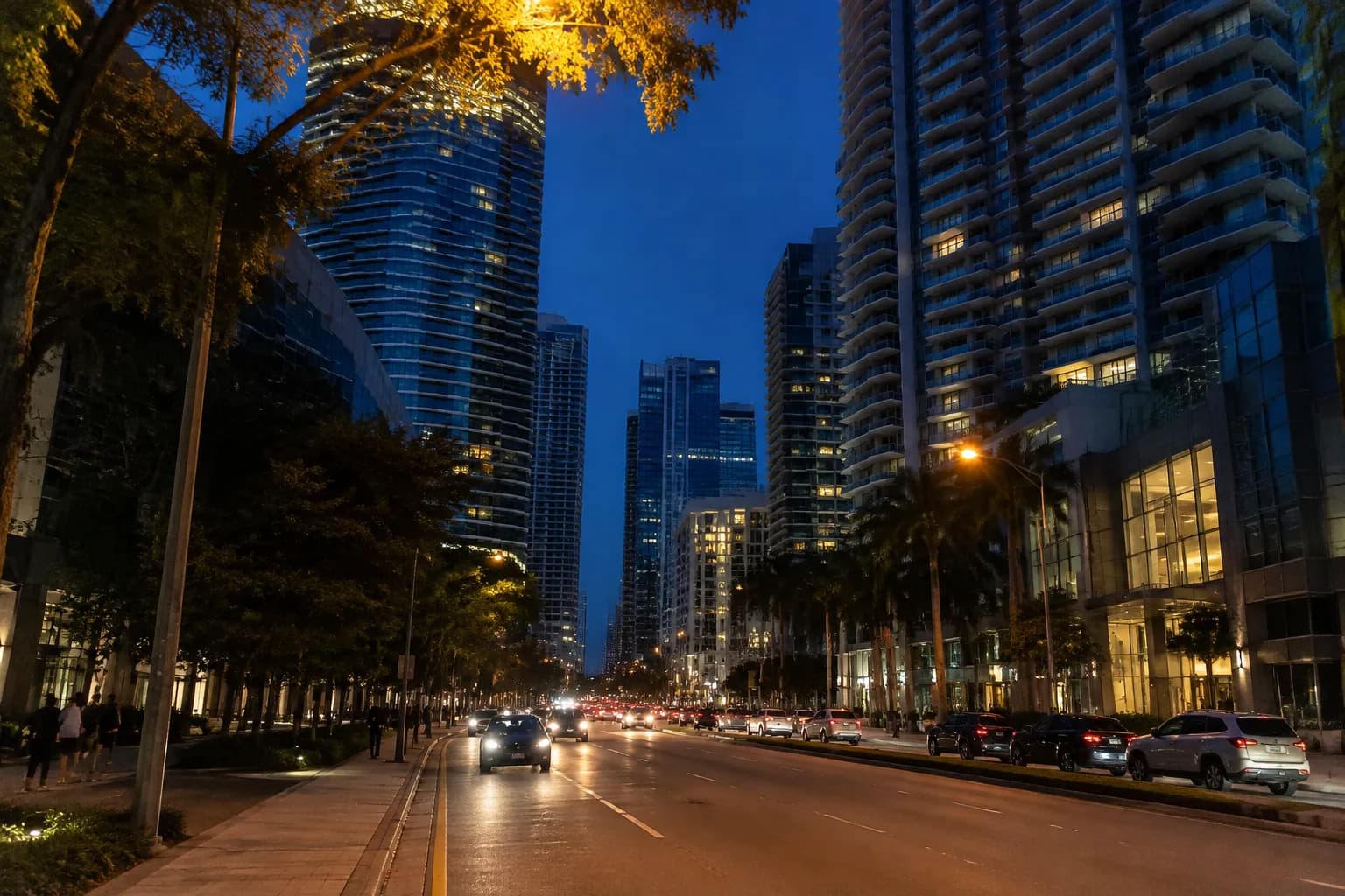 Brickell Avenue at dusk with residential towers, streetlights, and pedestrians on wide sidewalks