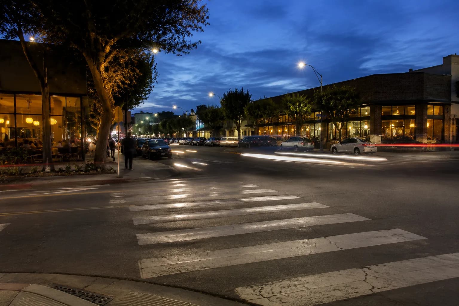 Culver City downtown intersection at dusk with lit restaurant windows and streetlights beginning to glow against a blue evening sky