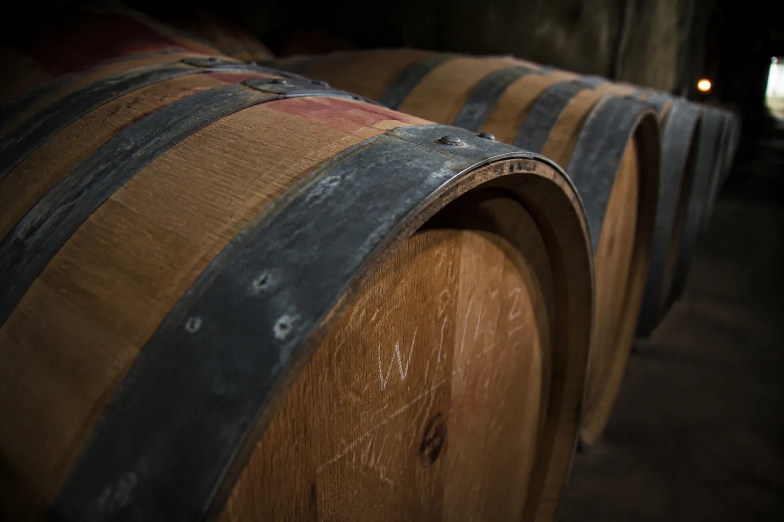 Oak wine barrels stacked in a California winery cellar with chalk markings visible