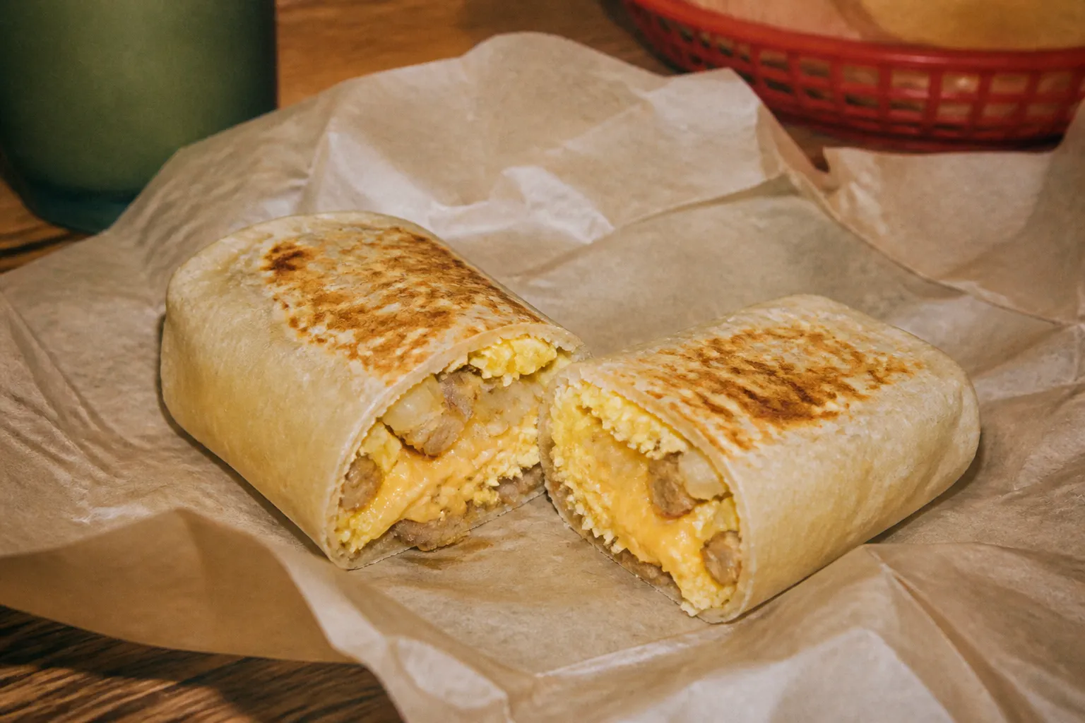 A wrapped breakfast burrito cut in half showing eggs and fillings on paper