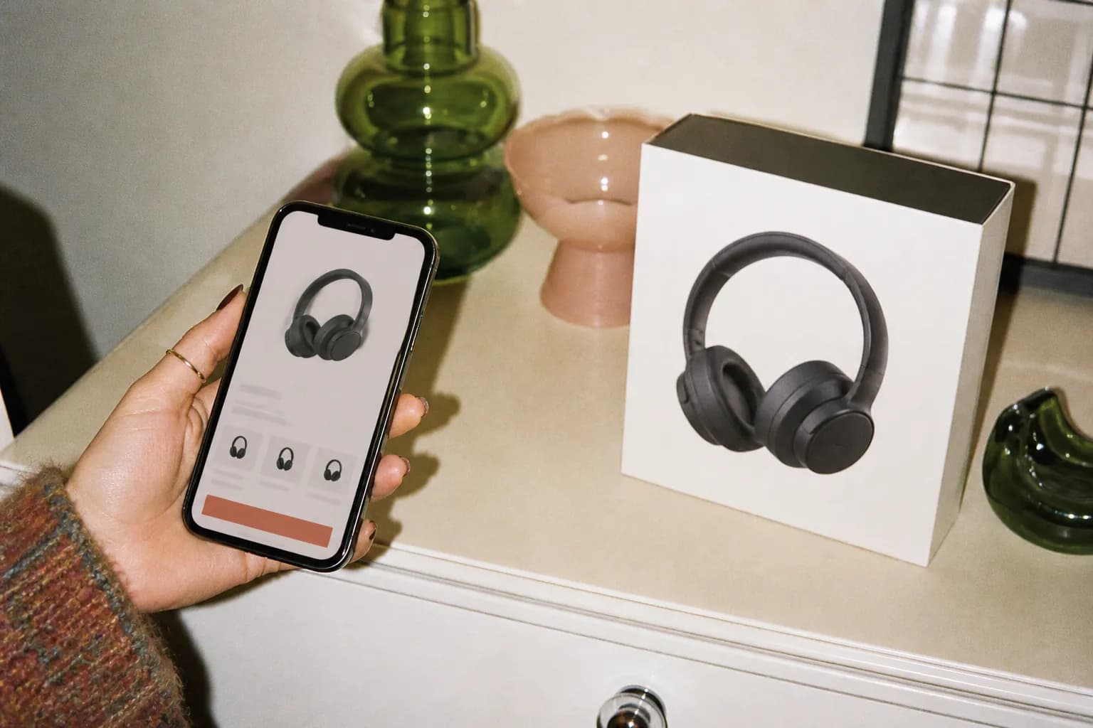 A phone showing a lower price held up beside a boxed electronics gadget