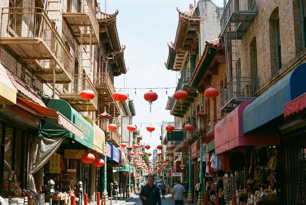 A narrow street of close-packed shopfronts with balconies above and lanterns strung between them, awnings crowding the pavement on both sides