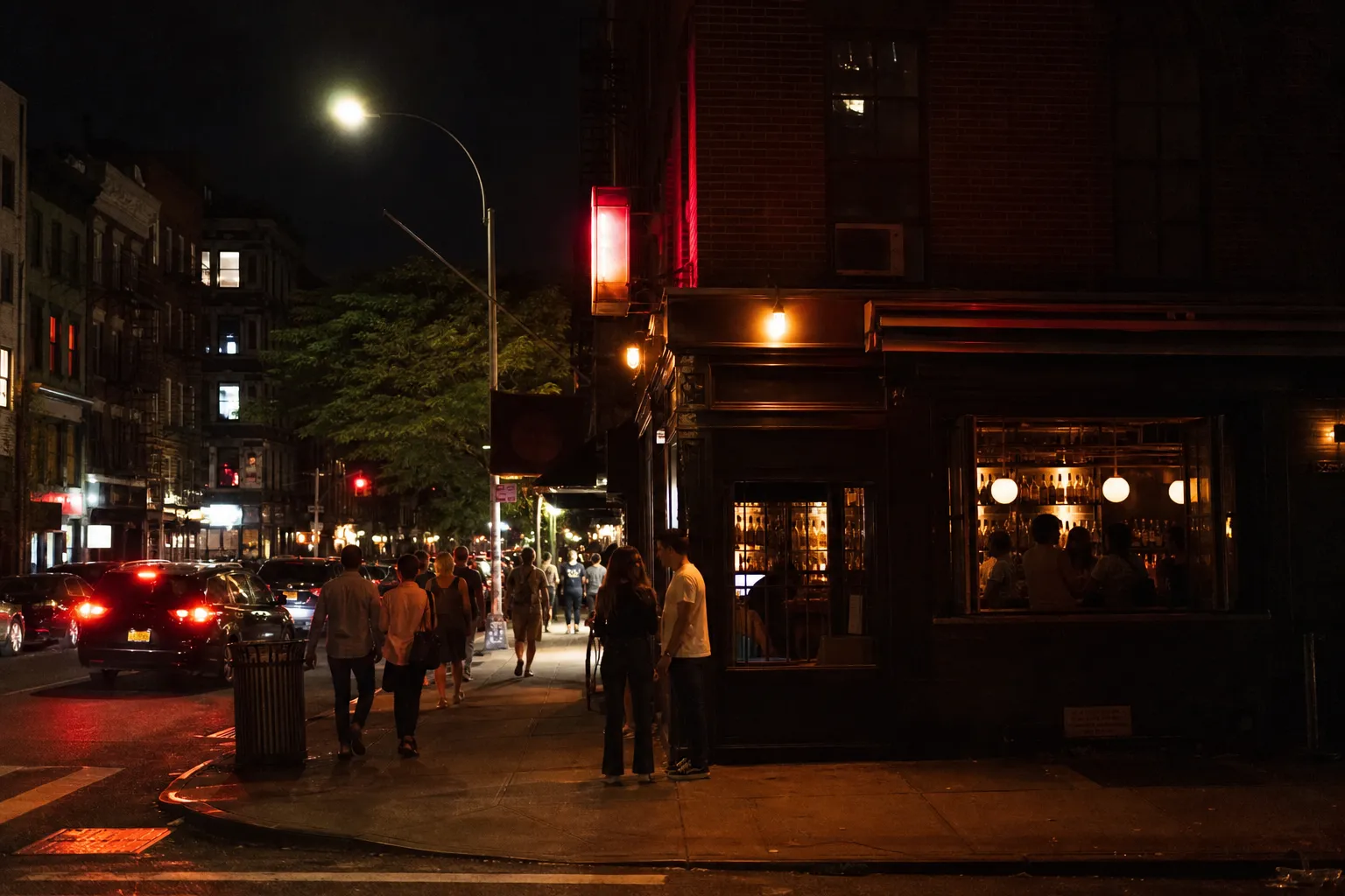 Lit East Village bar fronts on a lively corner at night