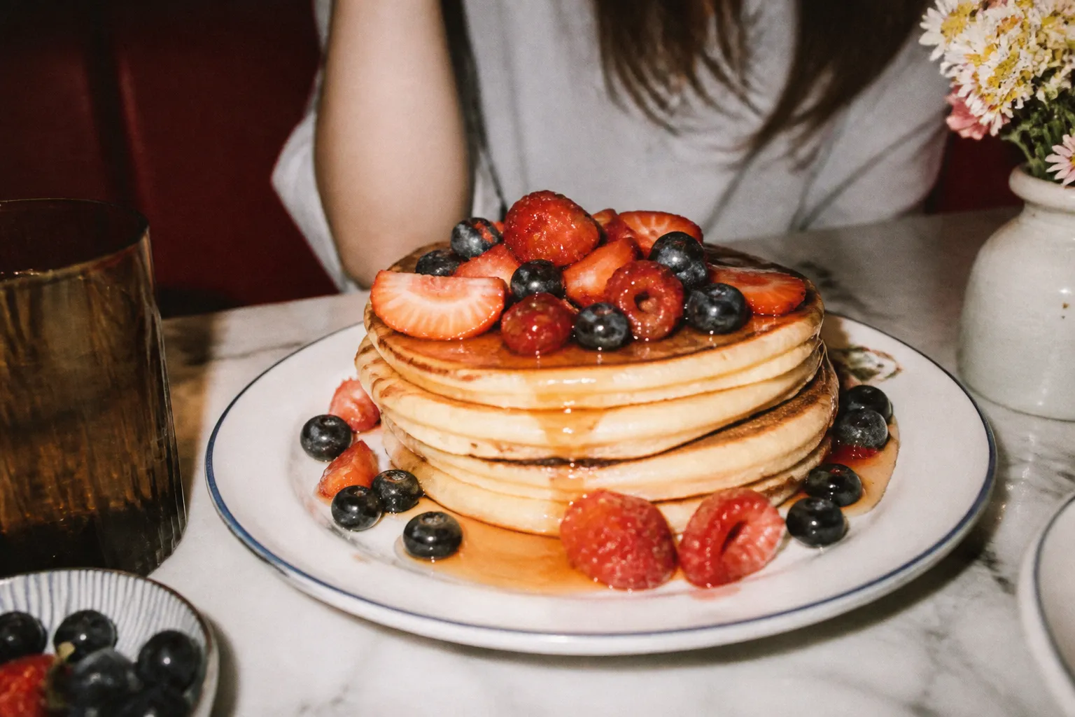 A tall stack of pancakes topped with syrup and fresh berries