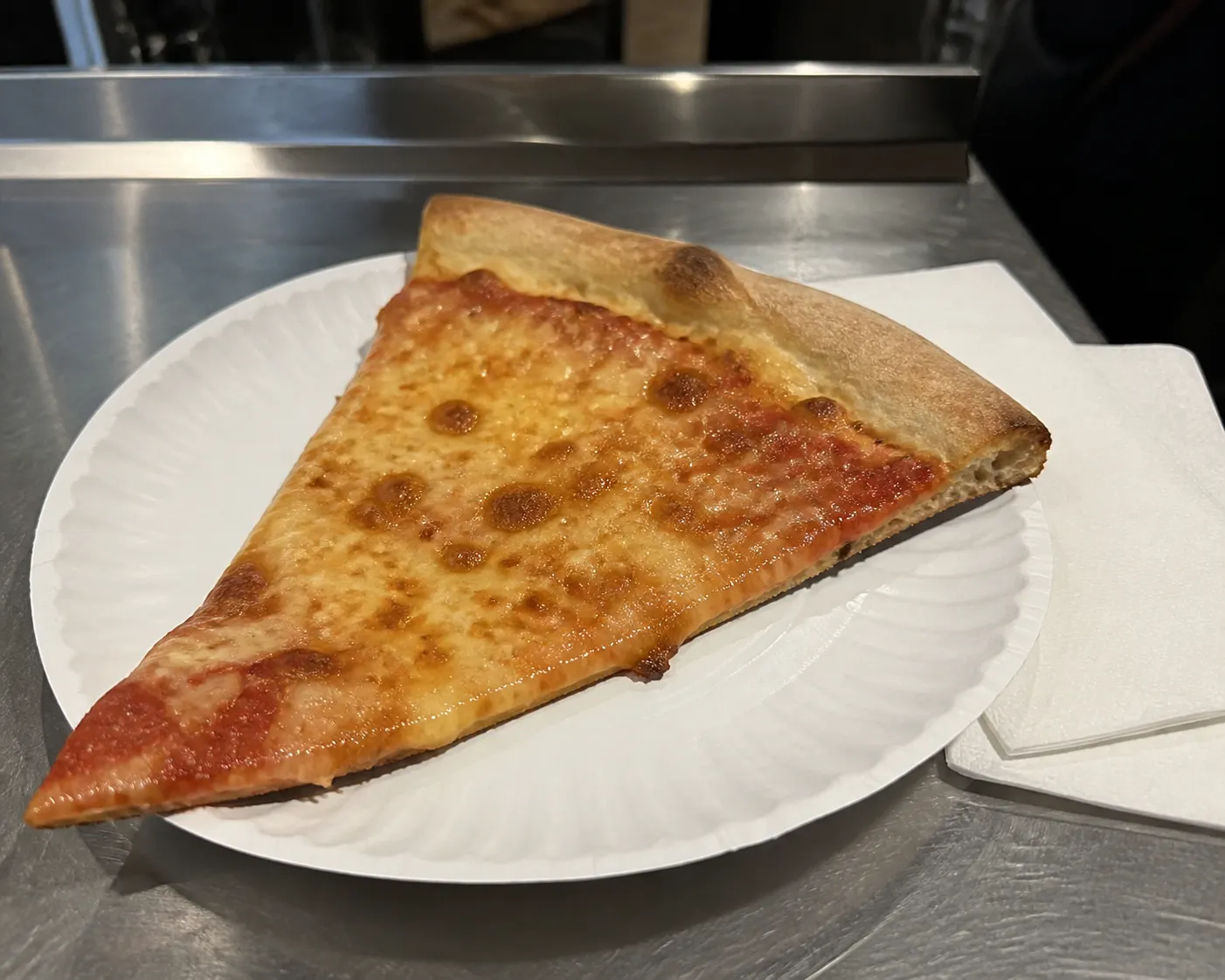 A hot folded cheese slice on a paper plate after midnight