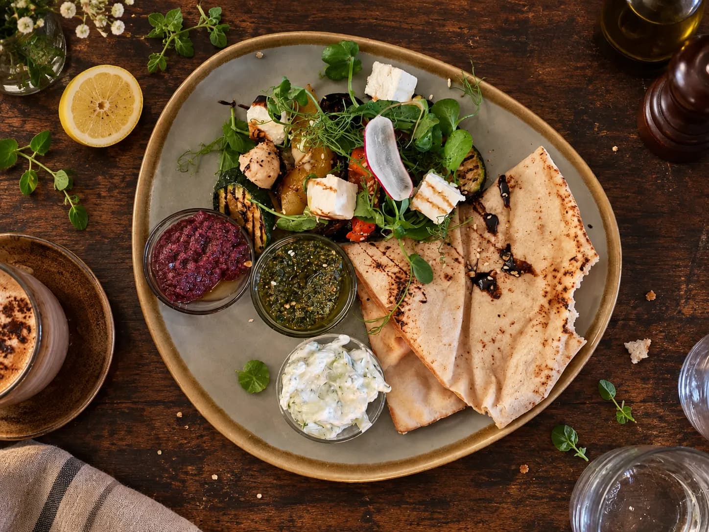 Large puffed flatbread torn at one edge surrounded by small bowls of spreads on a dark timber table