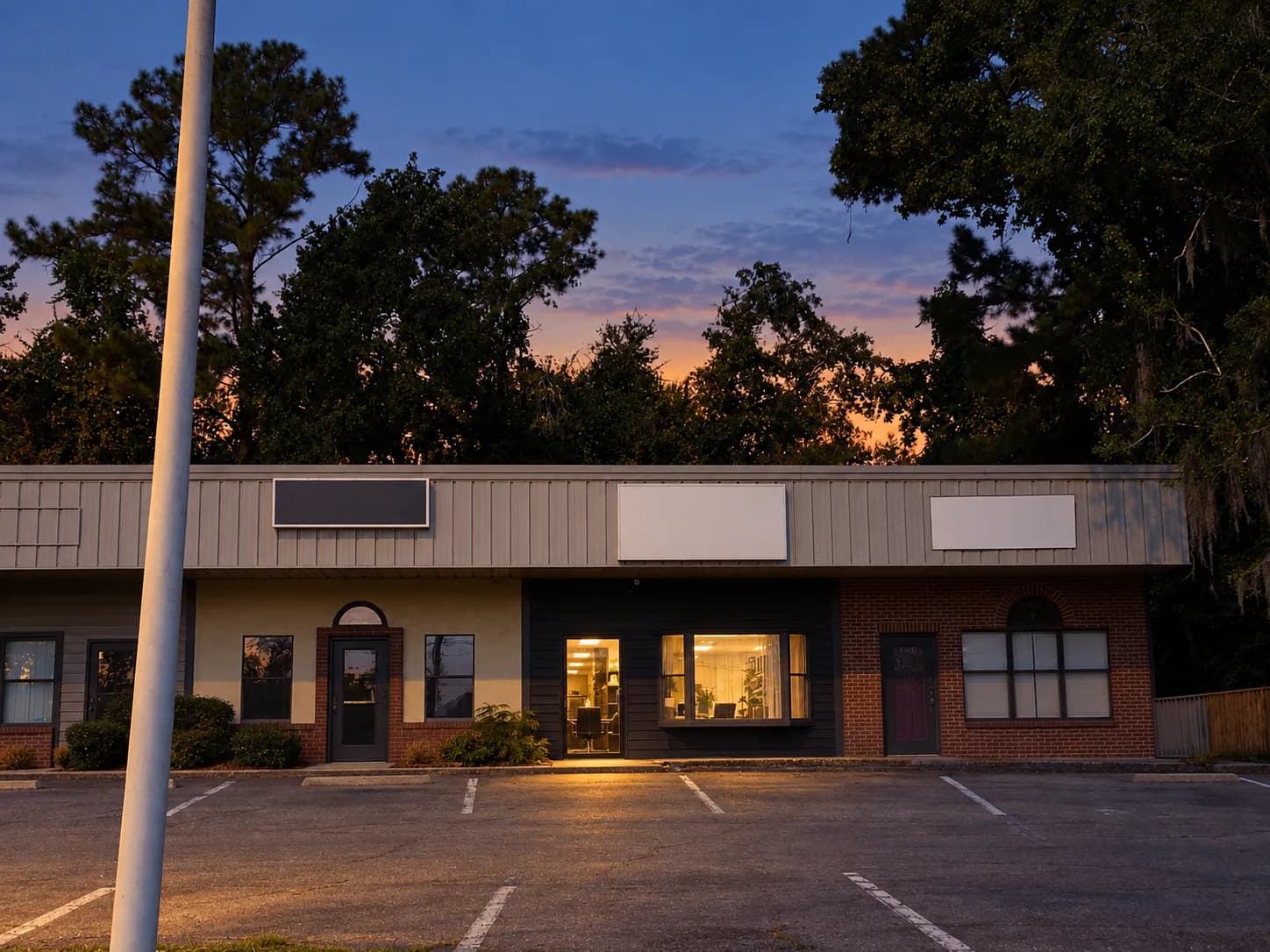 Low flat-roofed strip building at dusk with plate-glass shopfronts and one unit warmly lit from inside