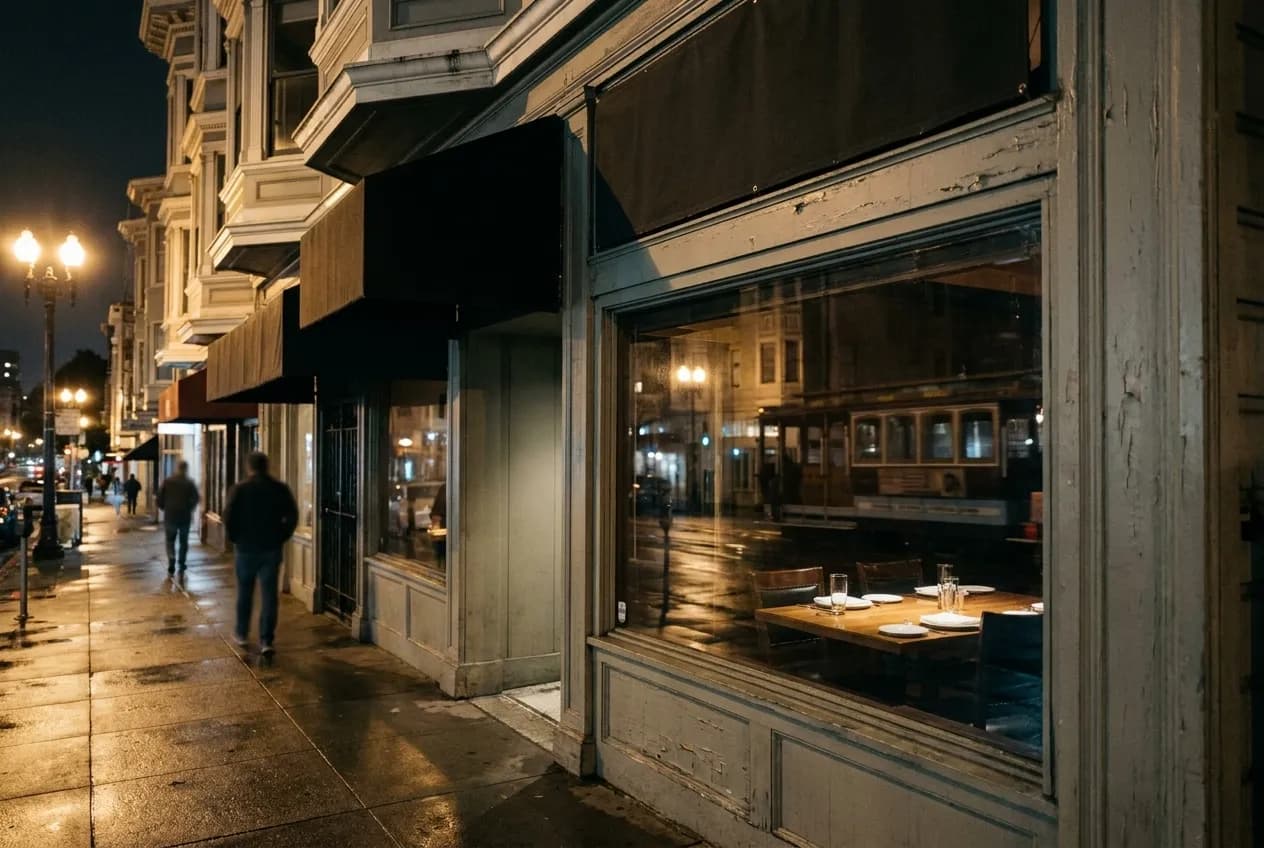 A restaurant window at night with a single table lit inside and the street reflected