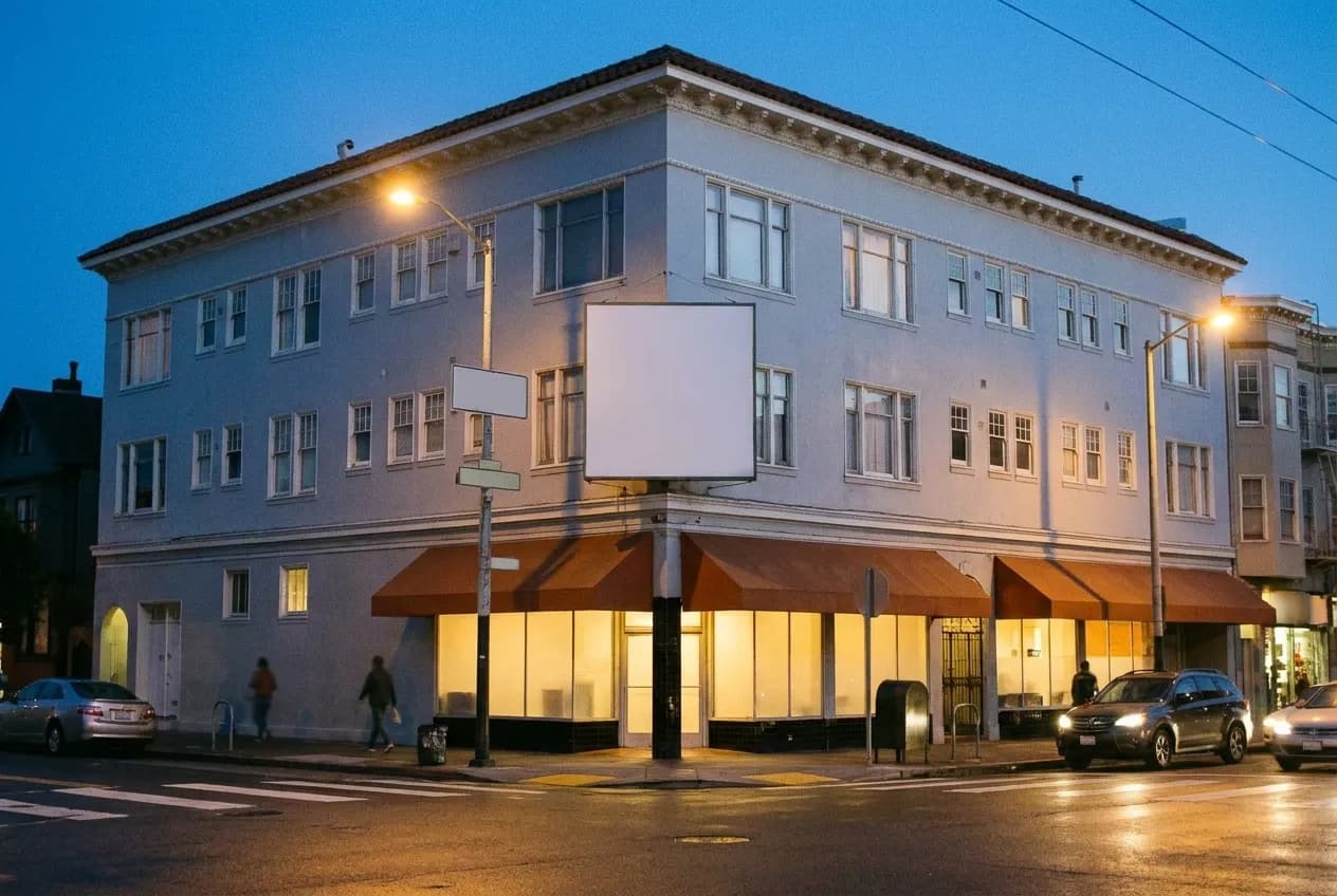 A commercial street corner in San Francisco at dusk with restaurant frontages and a crossing