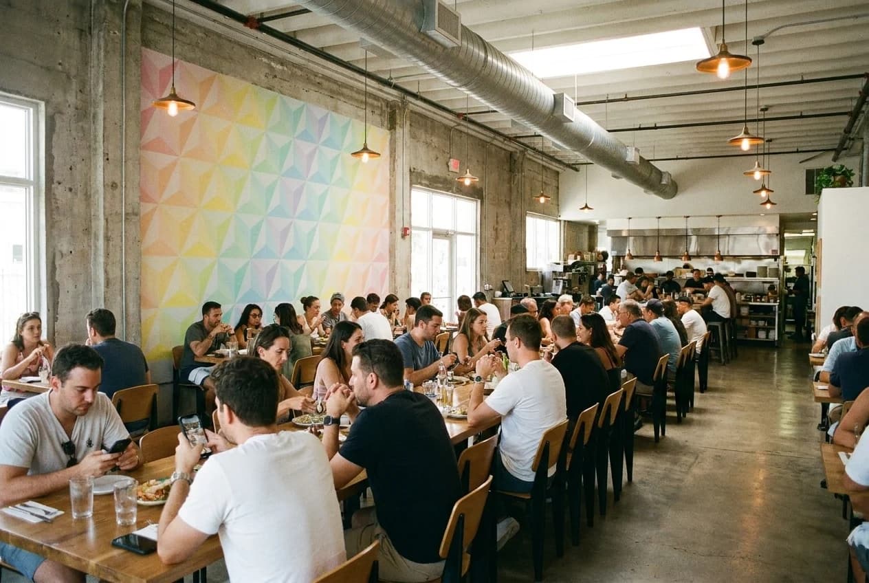 Wide interior view of a Wynwood warehouse restaurant dining room with exposed concrete walls and communal table