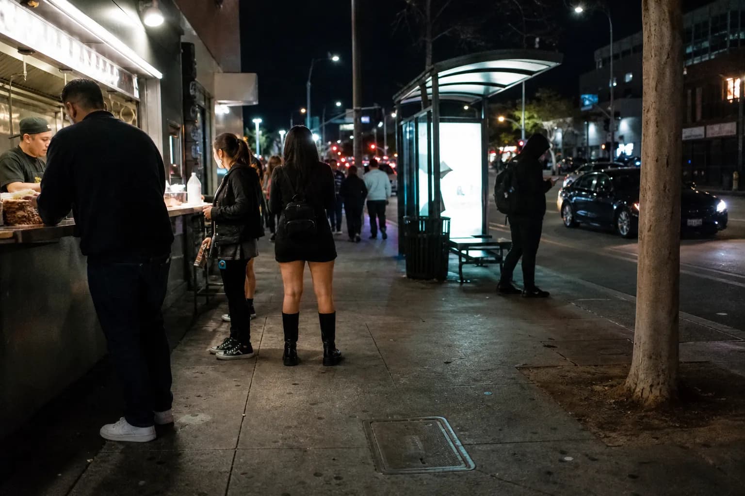 Late-night sidewalk scene near a bus stop and taco counter in Koreatown