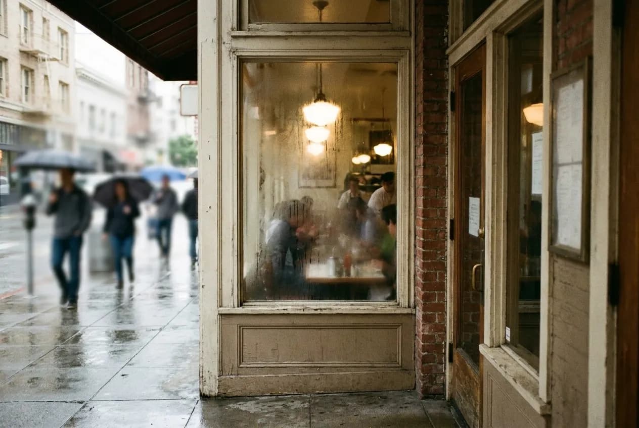 A narrow restaurant window fogged with steam from inside, hanging fixtures visible behind the glass and a strip of pavement below