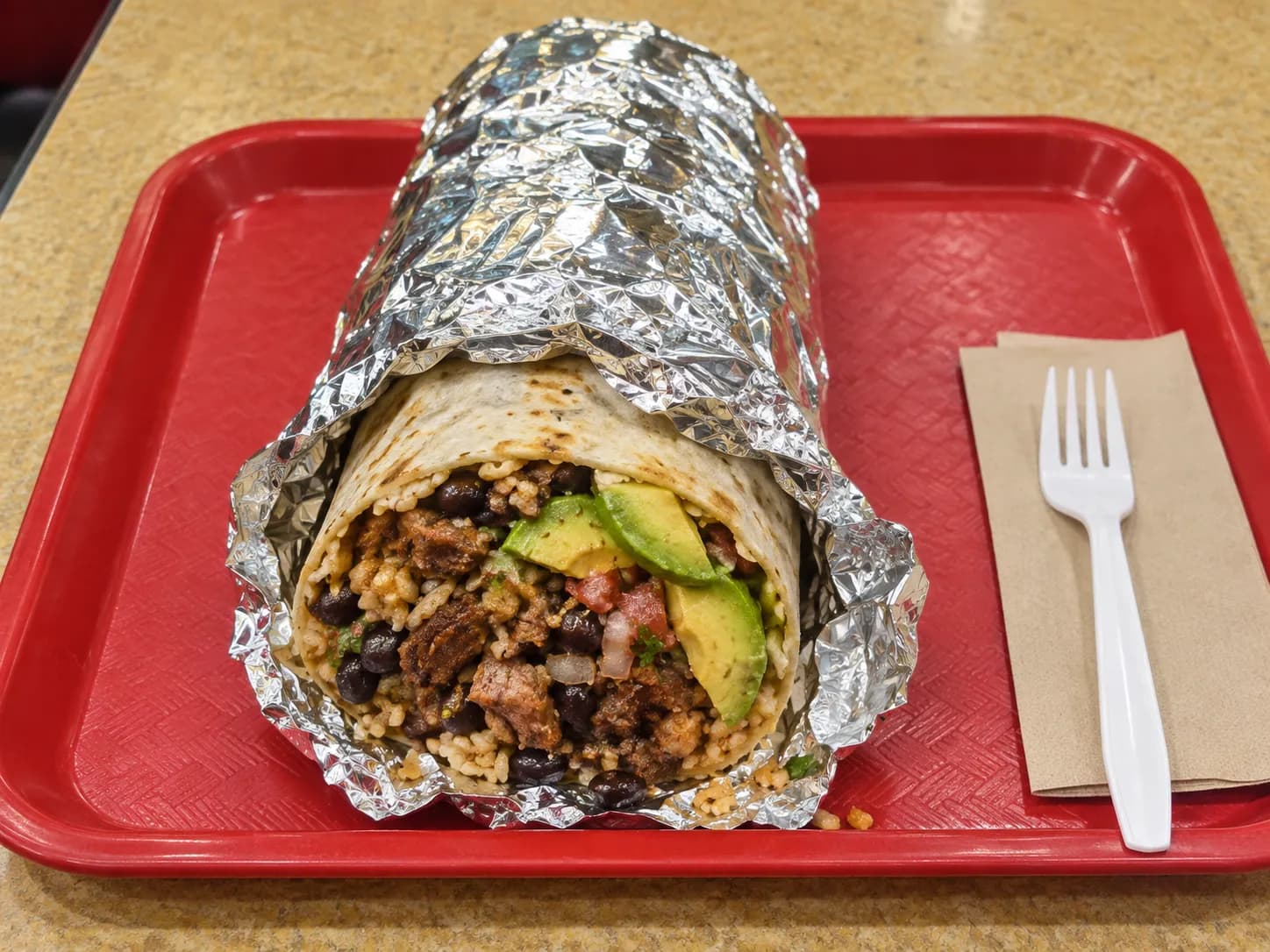 A foil-wrapped burrito unwrapped halfway on a tray