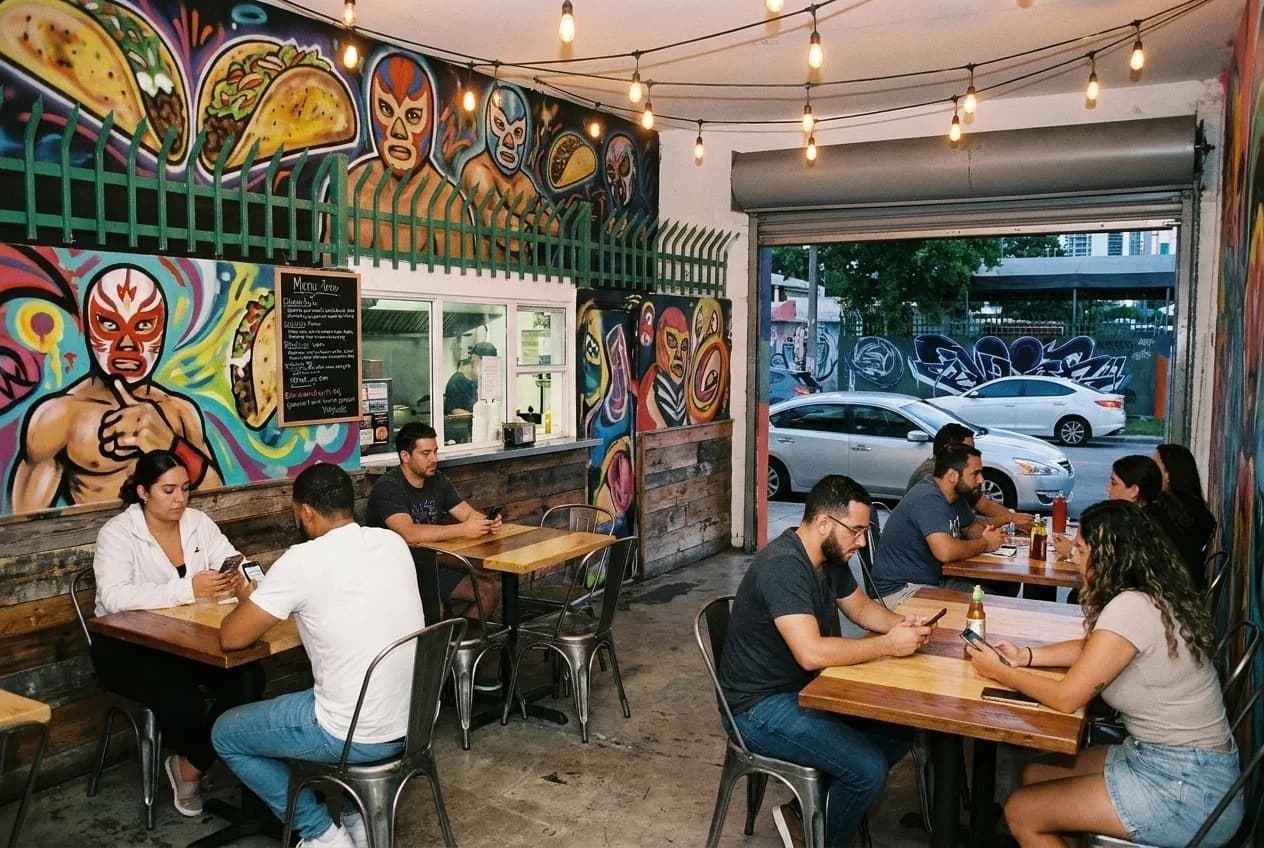 Bright counter-service taqueria interior in Wynwood with menu board and small tables under warm lighting