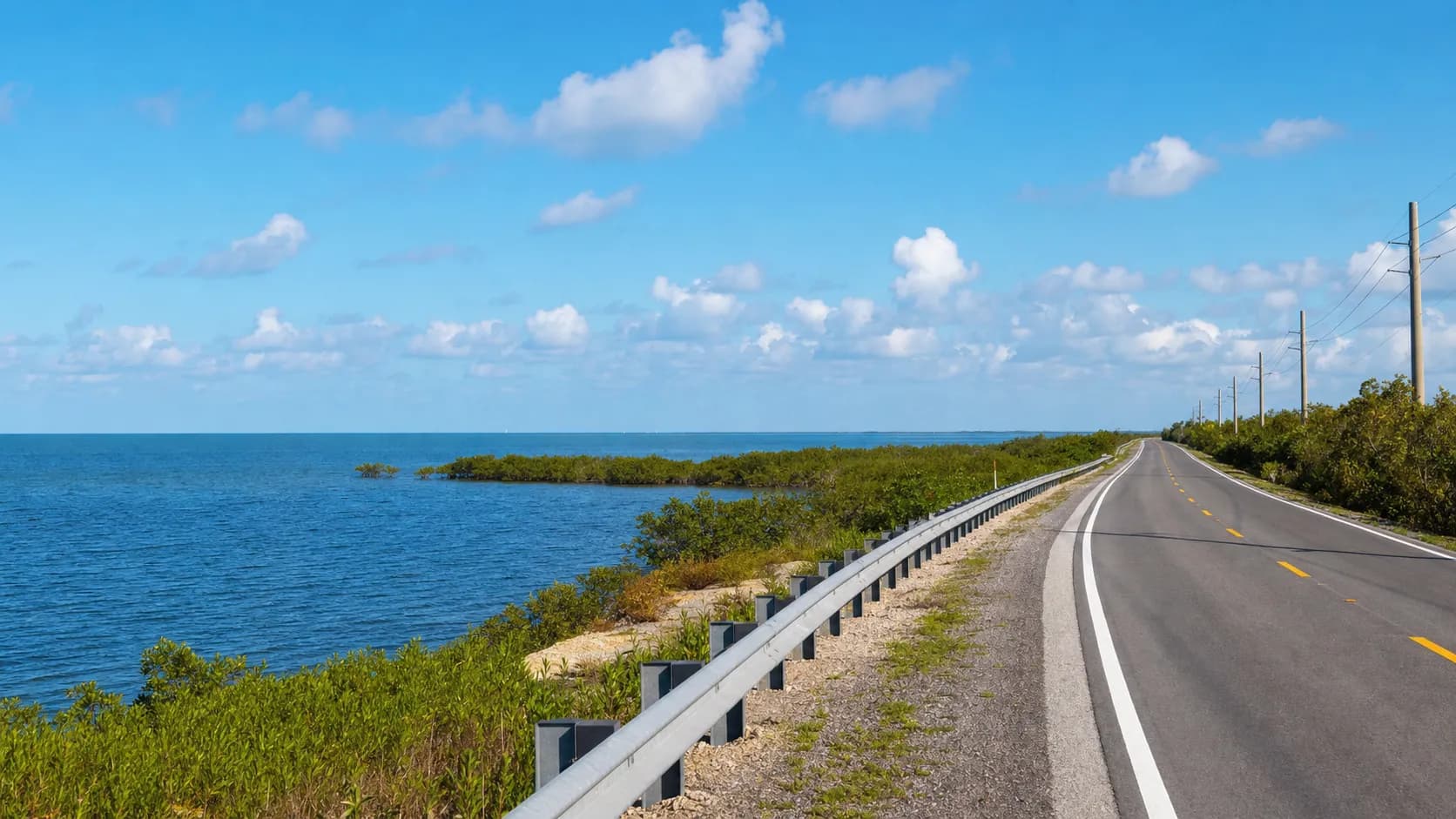 A sunny Florida Keys roadway stretches across water and low coastal vegetation.
