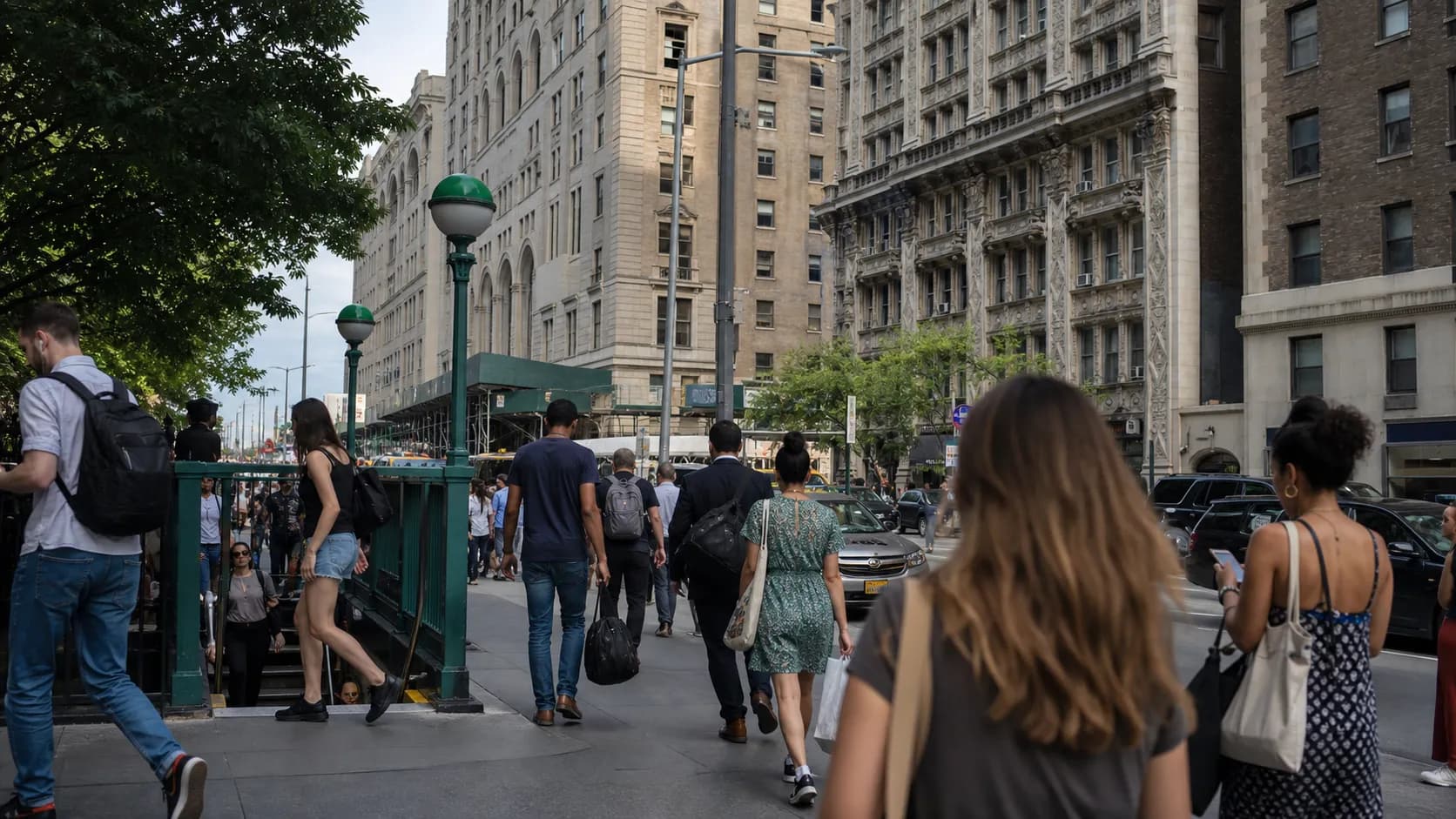 Commuters walk past a New York City subway entrance on a busy sidewalk.